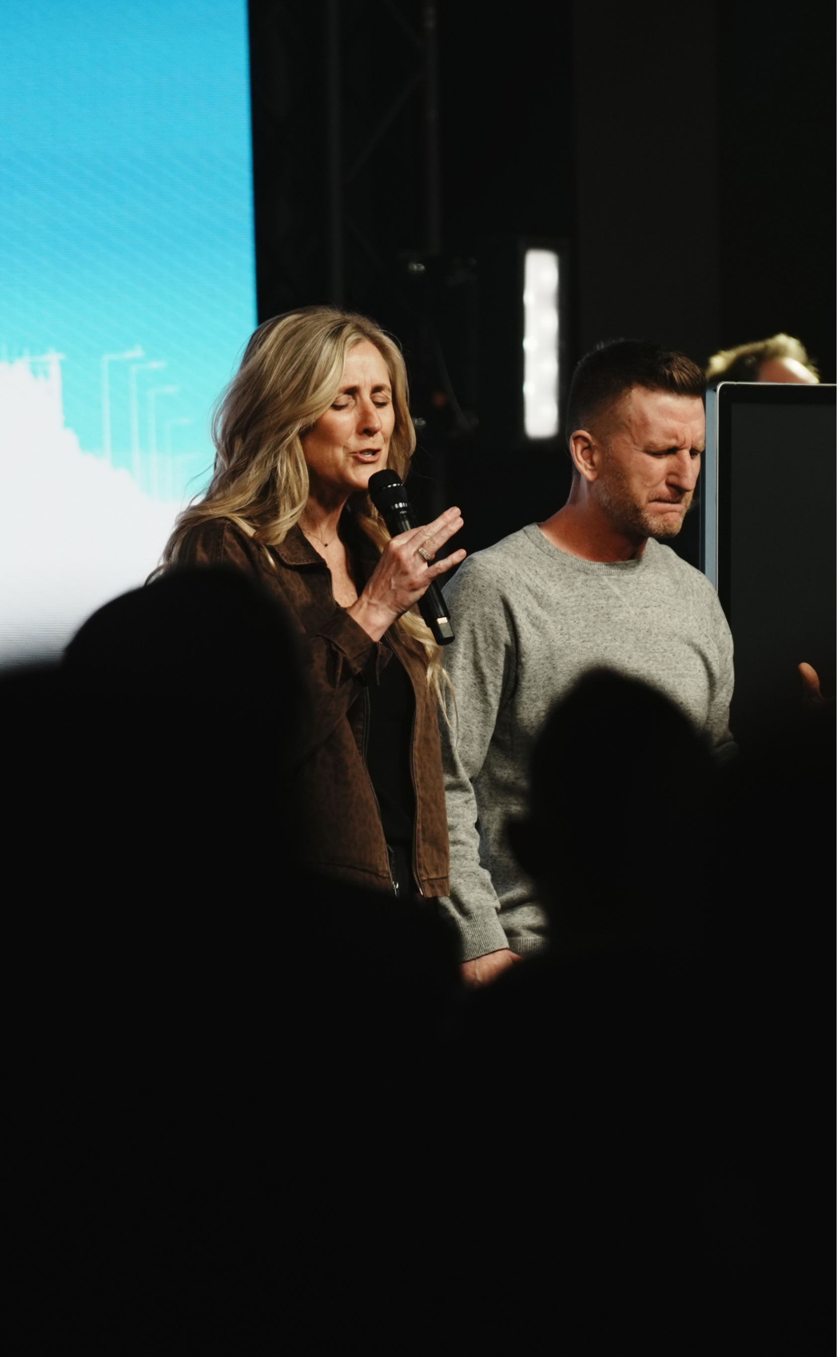 Pastors Bob and Cara Grimm praying on stage under the lights